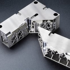 Das Bild zeigt zwei spiegelnde, silbernes Teil mit komplexen, gitterartigen inneren Strukturen. Sie sind teilweise ineinandergesteckt und liegen auf dunklem Grund.