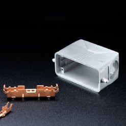  Das Bild zeigt ein geöffnetes, weißes Gehäuse für Elektronik, und daneben ein kupferfarbenes, metallisches Bauteil auf schwarzem Grund.